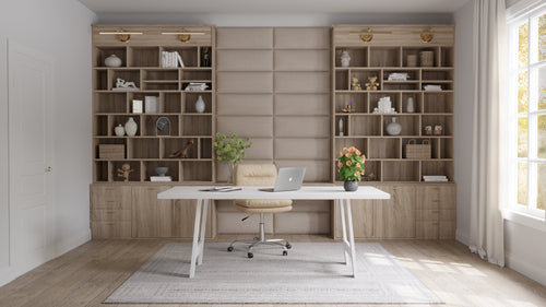 A modern home office featuring a vantpanel layout, with a white desk, laptop, beige upholstered wall, and wooden shelving units filled with books and decor.