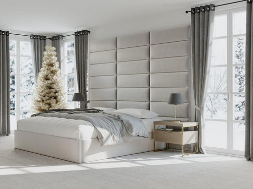 A modern bedroom with a large padded headboard and vantpanel panels, decorated for the holidays with a Christmas tree by the window.